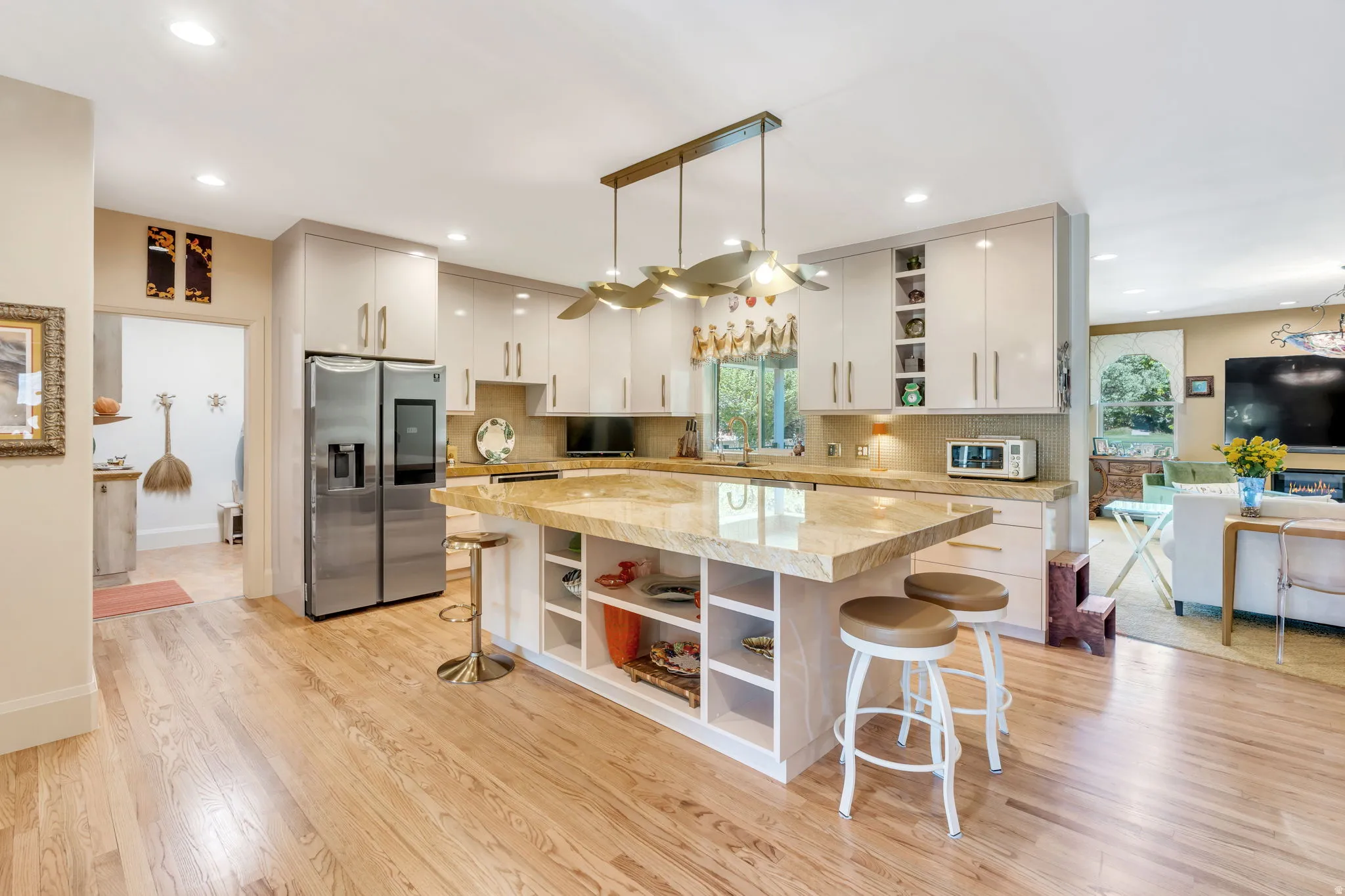 Modern kitchen featuring light wood-finish flooring, an expansive island with a light-toned countertop, sleek flat-panel cabinetry, recessed lighting, and stainless steel appliances