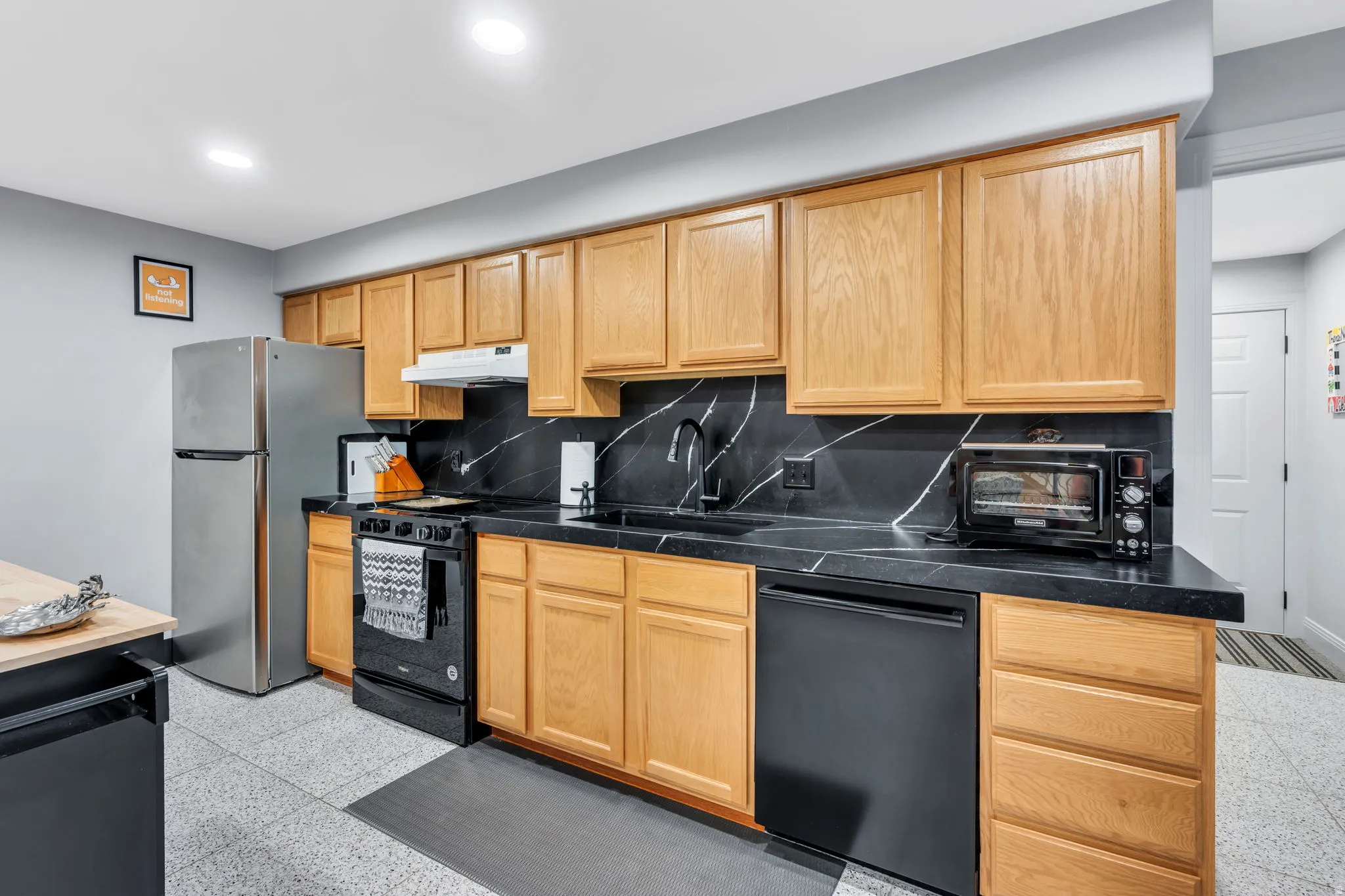 Kitchen featuring light wood cabinetry, a black counter, and a black and white marble-look backsplash