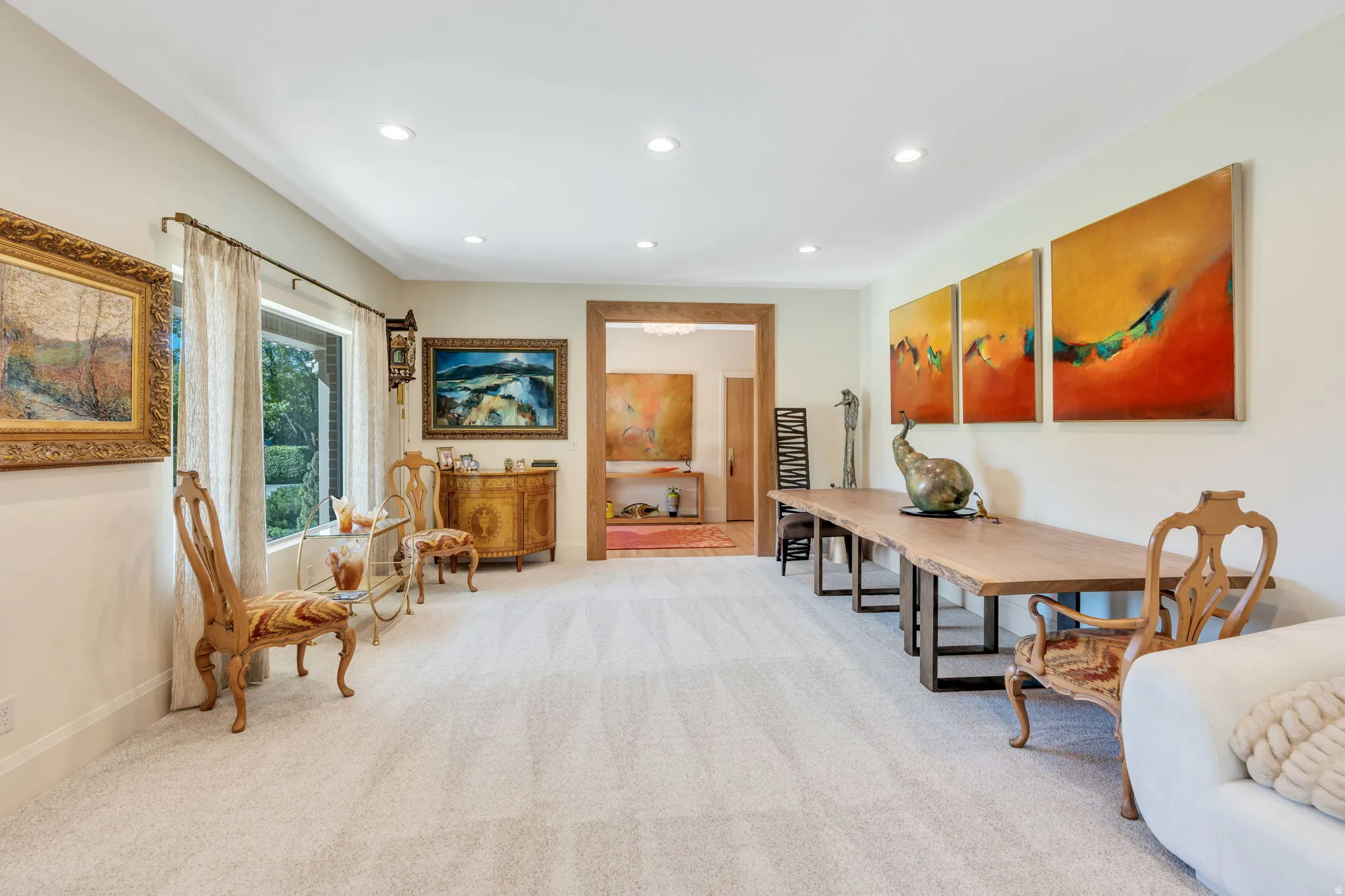 Recessed lighting illuminates this bright room featuring light-colored carpeting, a large picture window with drapes, and a wide wooden archway