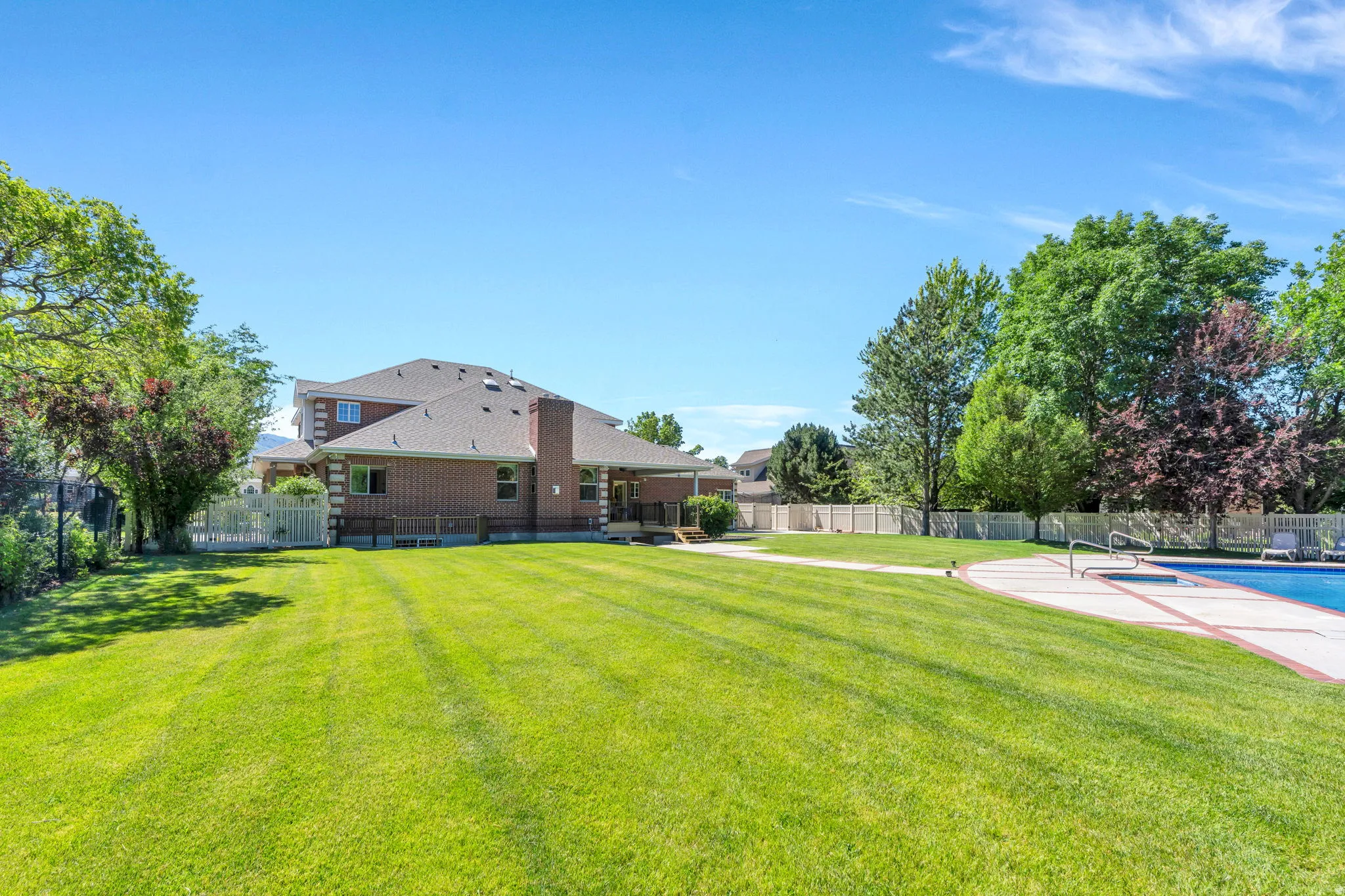 Expansive backyard featuring a manicured lawn, a swimming pool with integrated spa, and mature trees