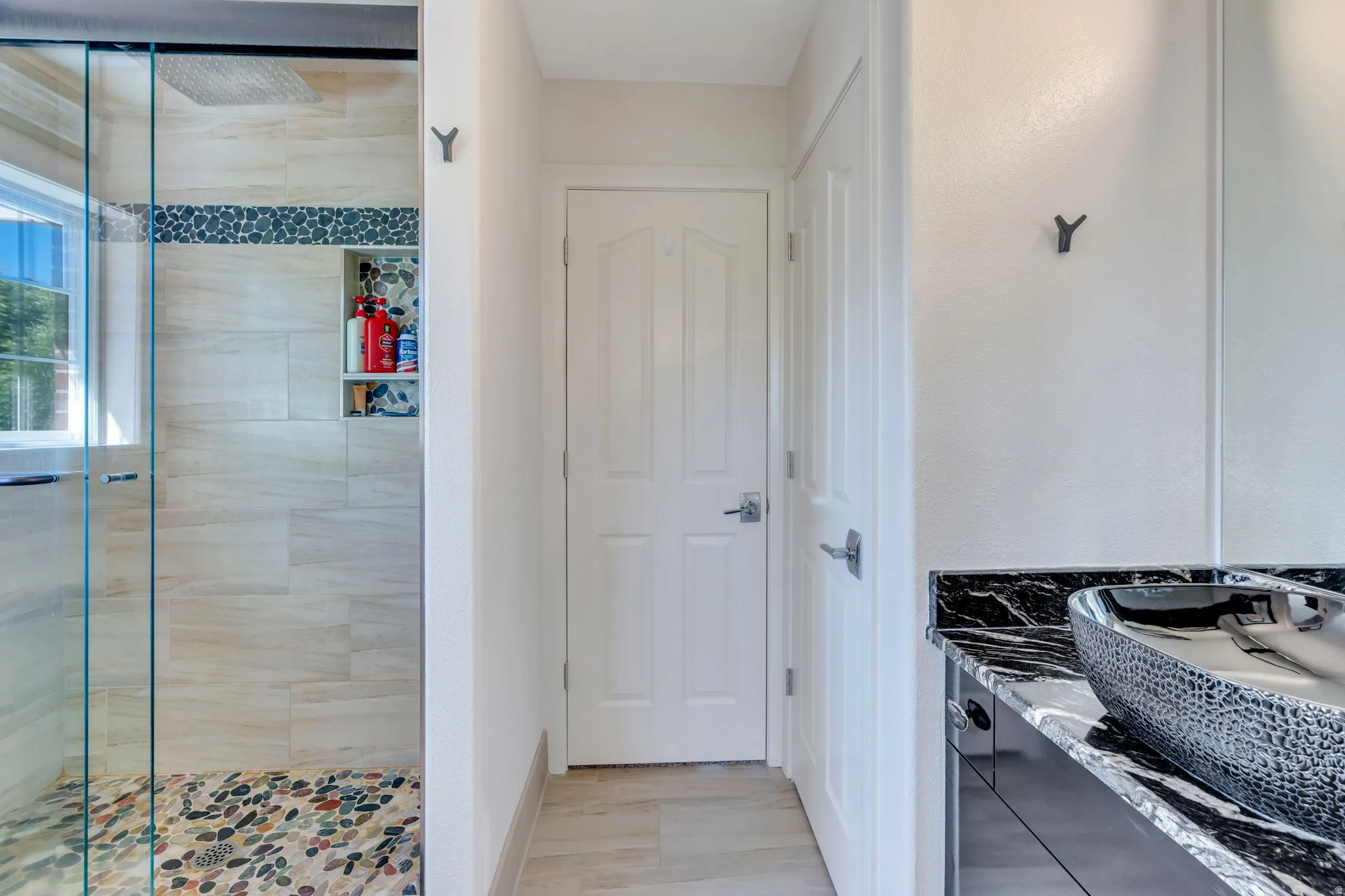 Bathroom featuring a glass-enclosed shower with pebble-tile flooring, a recessed shower niche, and light-toned wall tiling