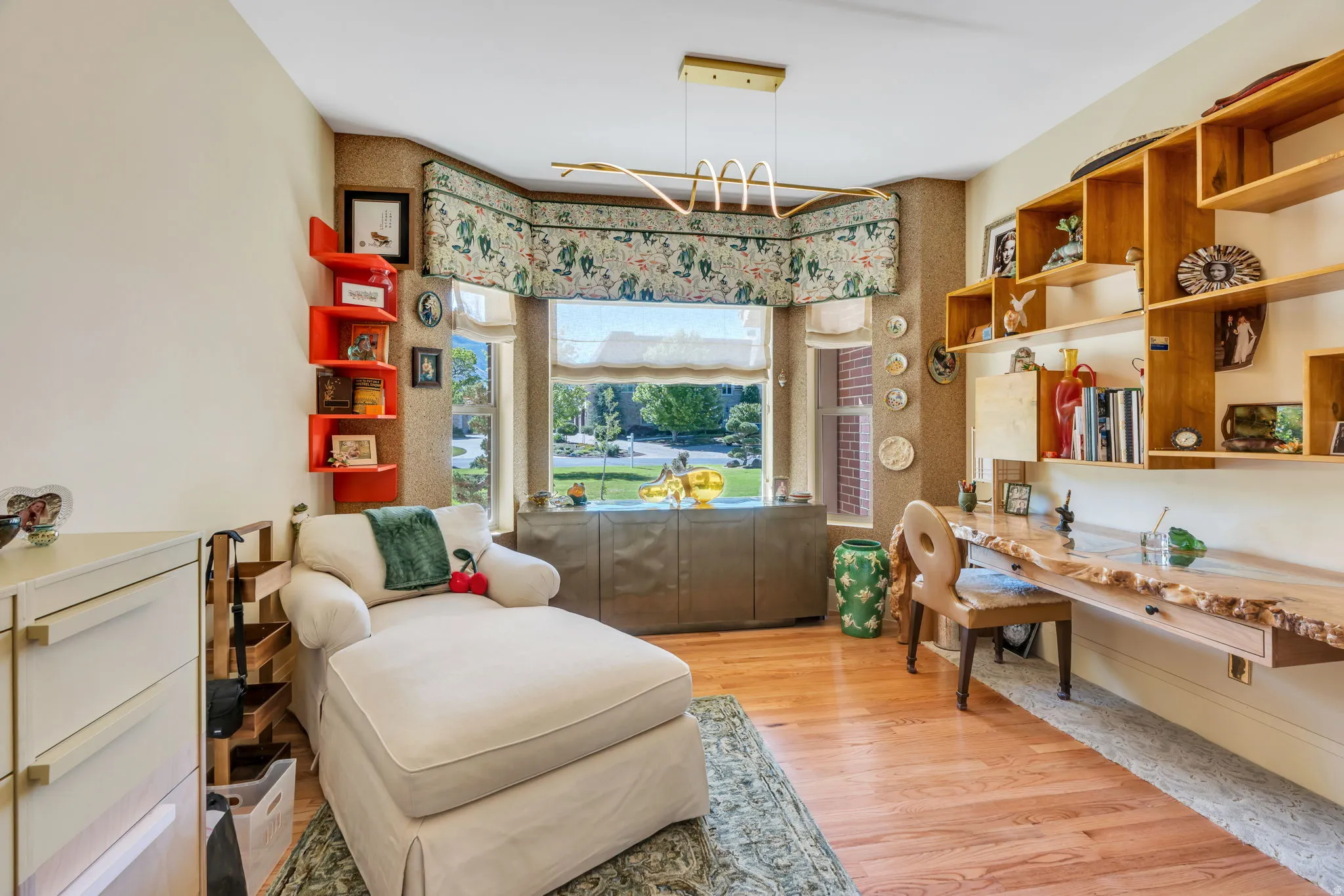 Room featuring wood-finish flooring, a prominent bay window with custom valance, a built-in live edge wood desk with integrated shelving, and a modern linear chandelier