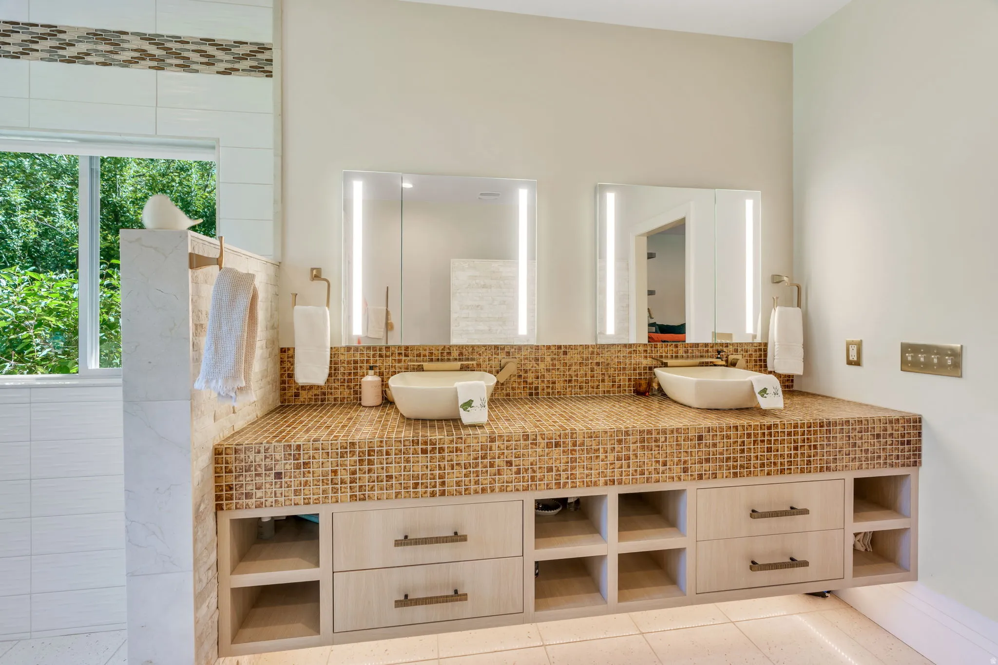 Dual vessel sinks set into a mosaic tile countertop, complemented by two integrated-light medicine cabinet mirrors