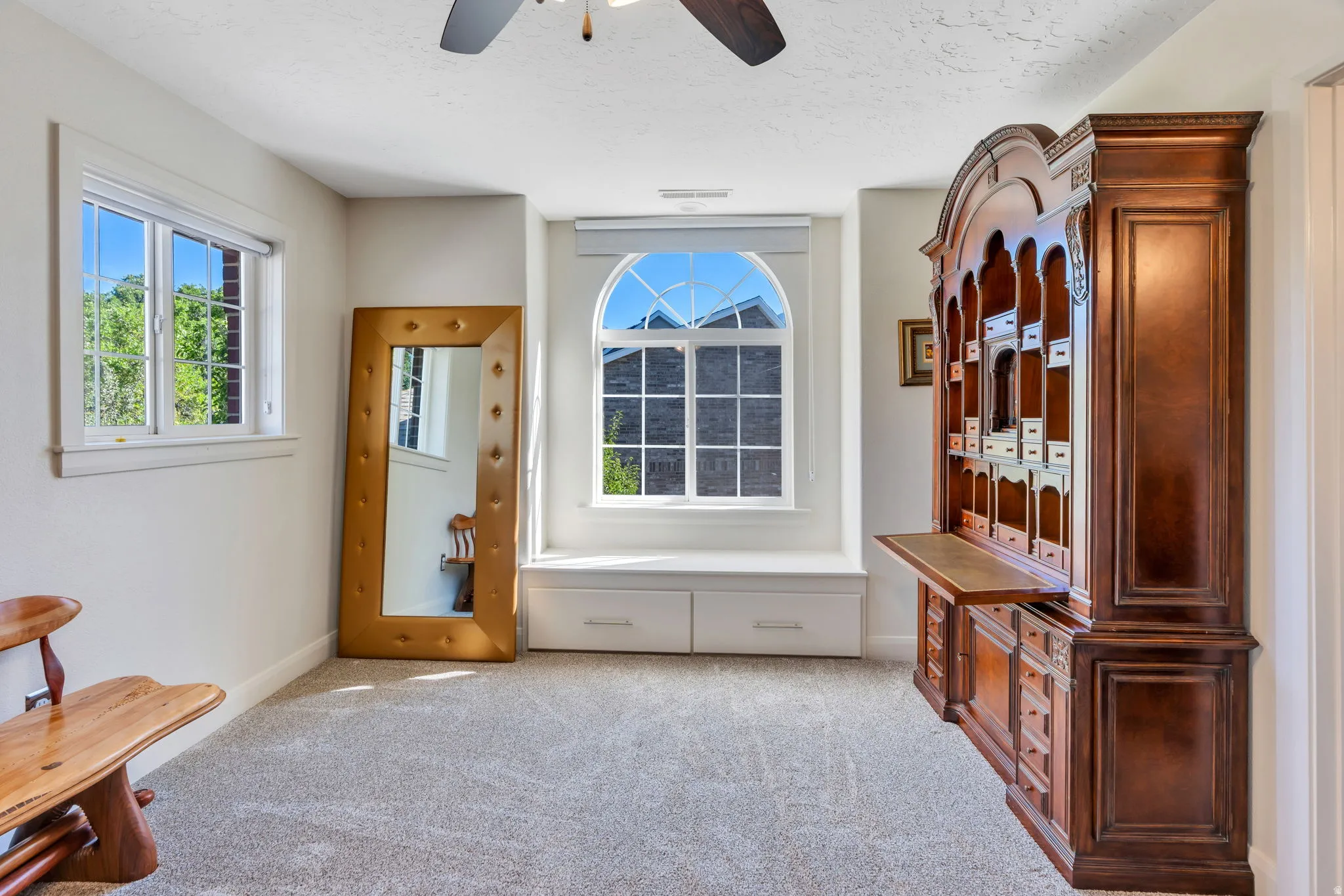 Carpeted room featuring a ceiling fan, two windows with exterior views, and a built-in window seat with integrated storage drawers