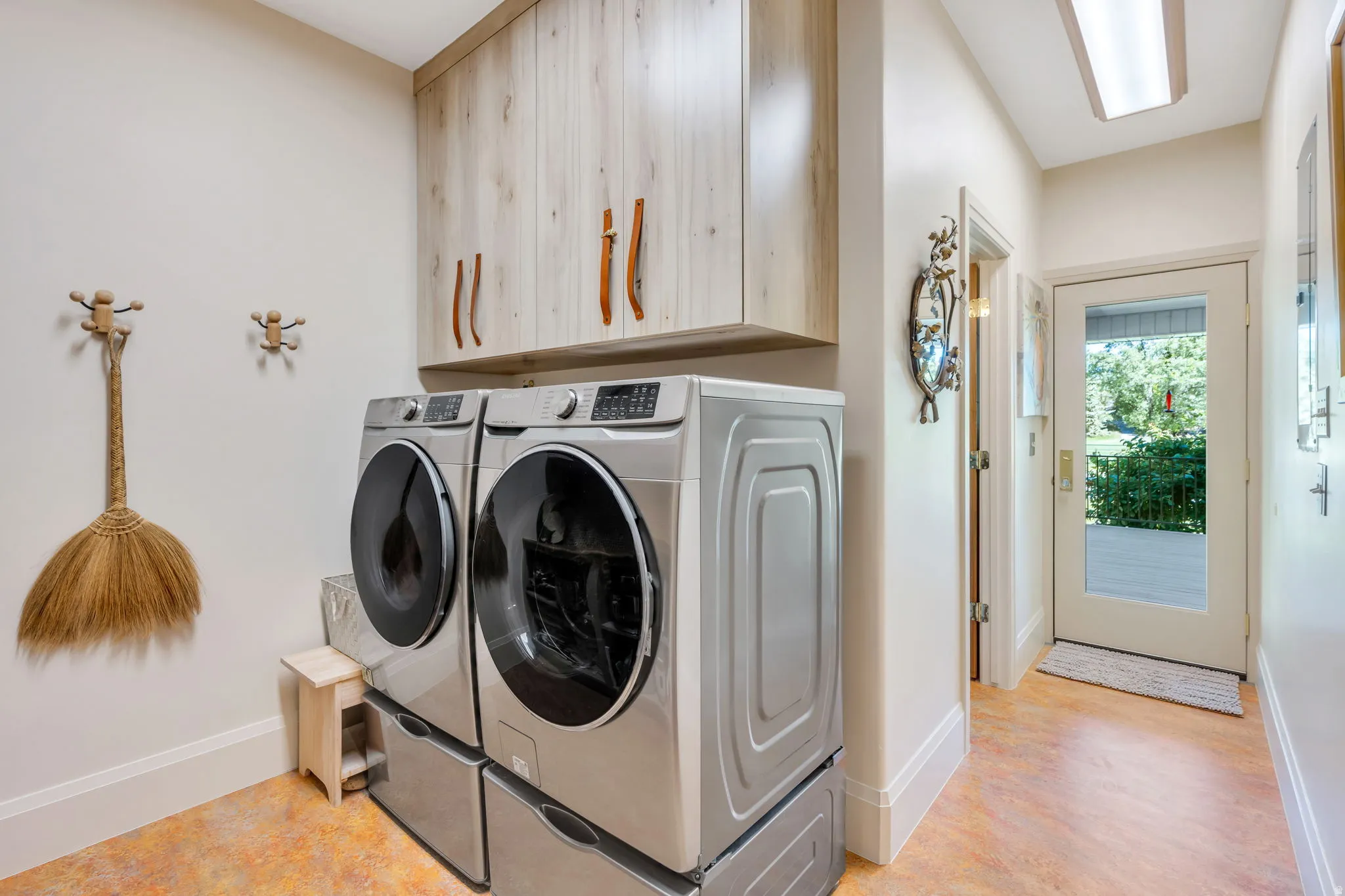 Dedicated laundry area featuring light wood-finish cabinetry with curved wood hardware, modern front-load appliances on pedestals, and a neutral color palette