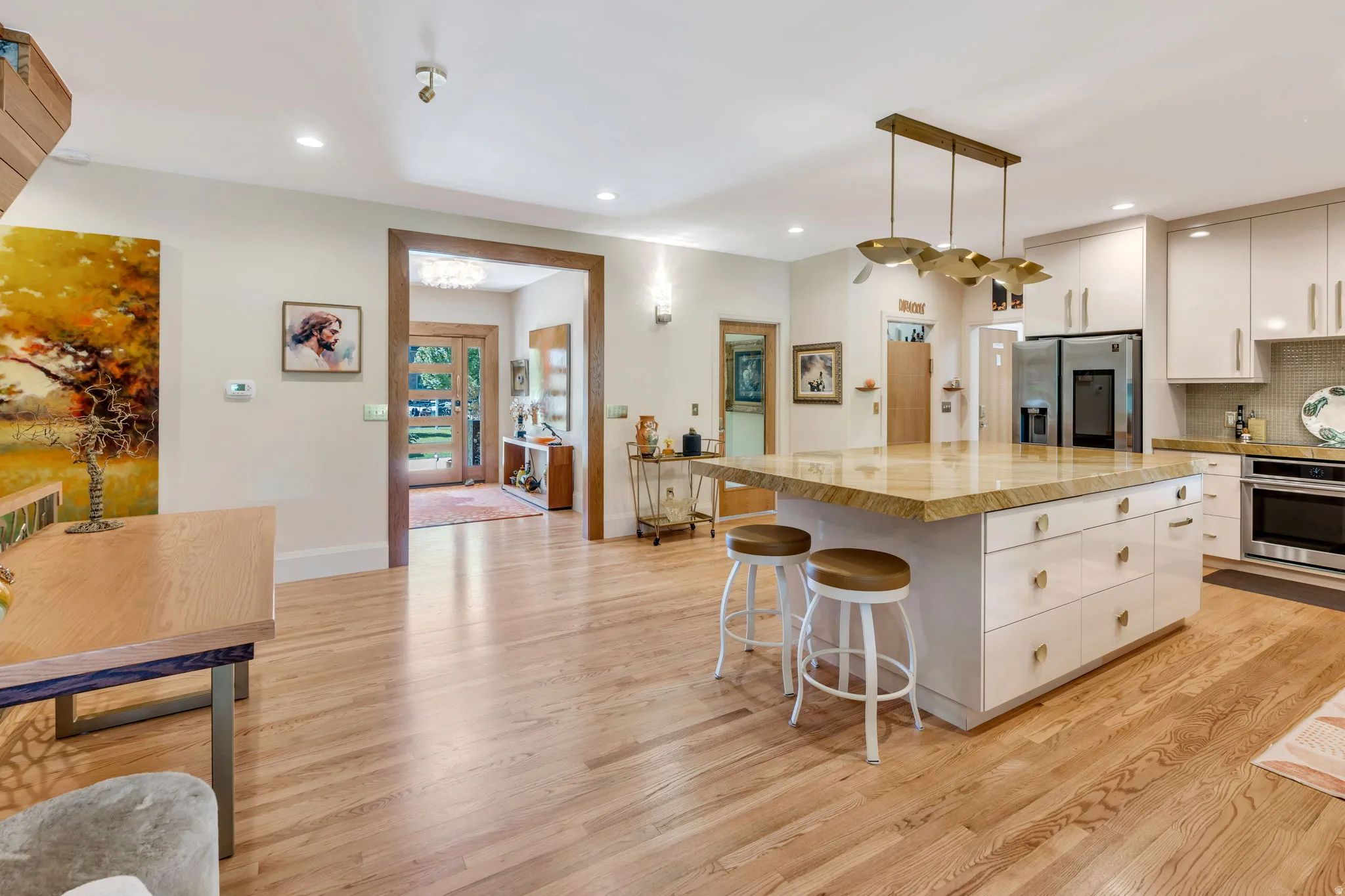 Open concept kitchen featuring a large central island with a stone countertop, white cabinetry with gold-toned hardware, and wood-finish flooring