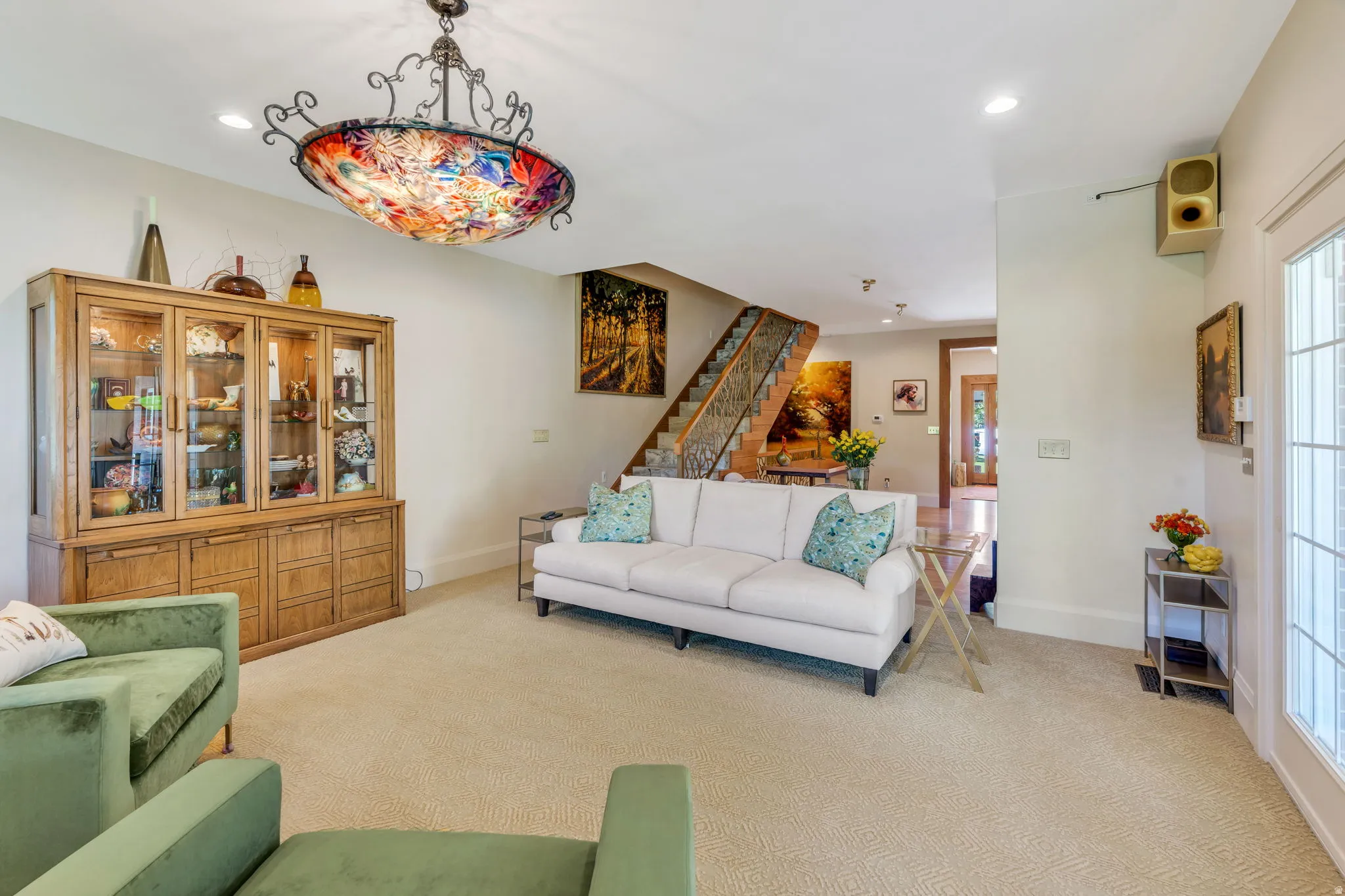 Spacious living area featuring a decorative overhead light fixture, light-toned carpet flooring, and a built-in wood display cabinet