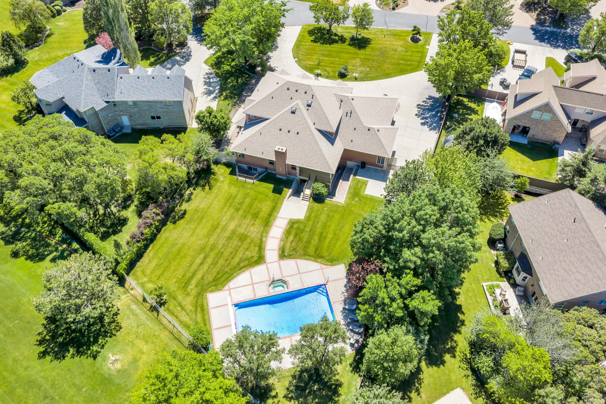 Expansive property featuring a large inground swimming pool with surrounding patio, a concrete driveway, and substantial green space with mature trees