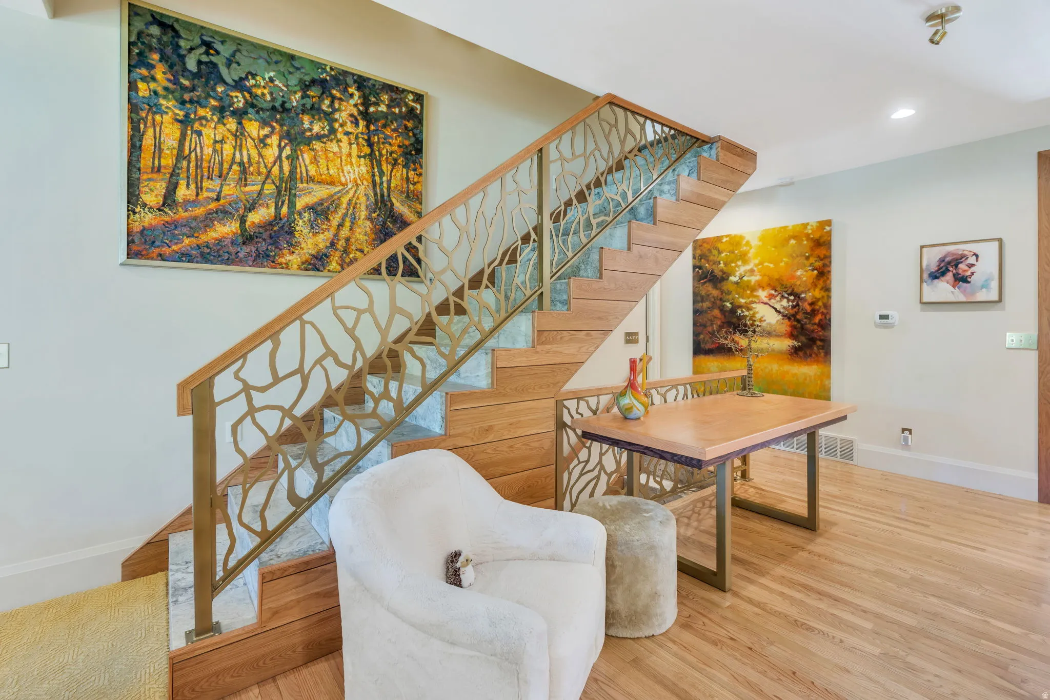 Hardwood flooring complements a custom staircase featuring a branch-patterned metal railing and stone risers