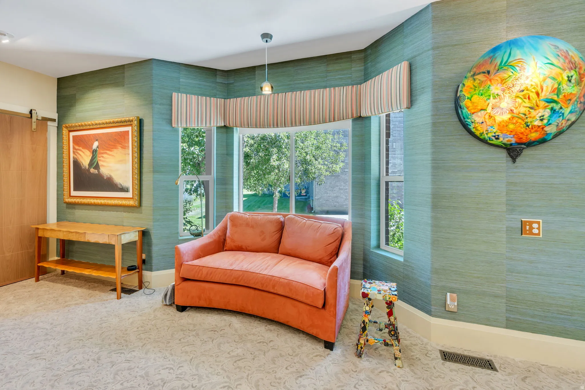 Bay window with striped valance, green grasscloth wallpaper, carpeted flooring, wood-finish interior door, and a built-in wall sconce