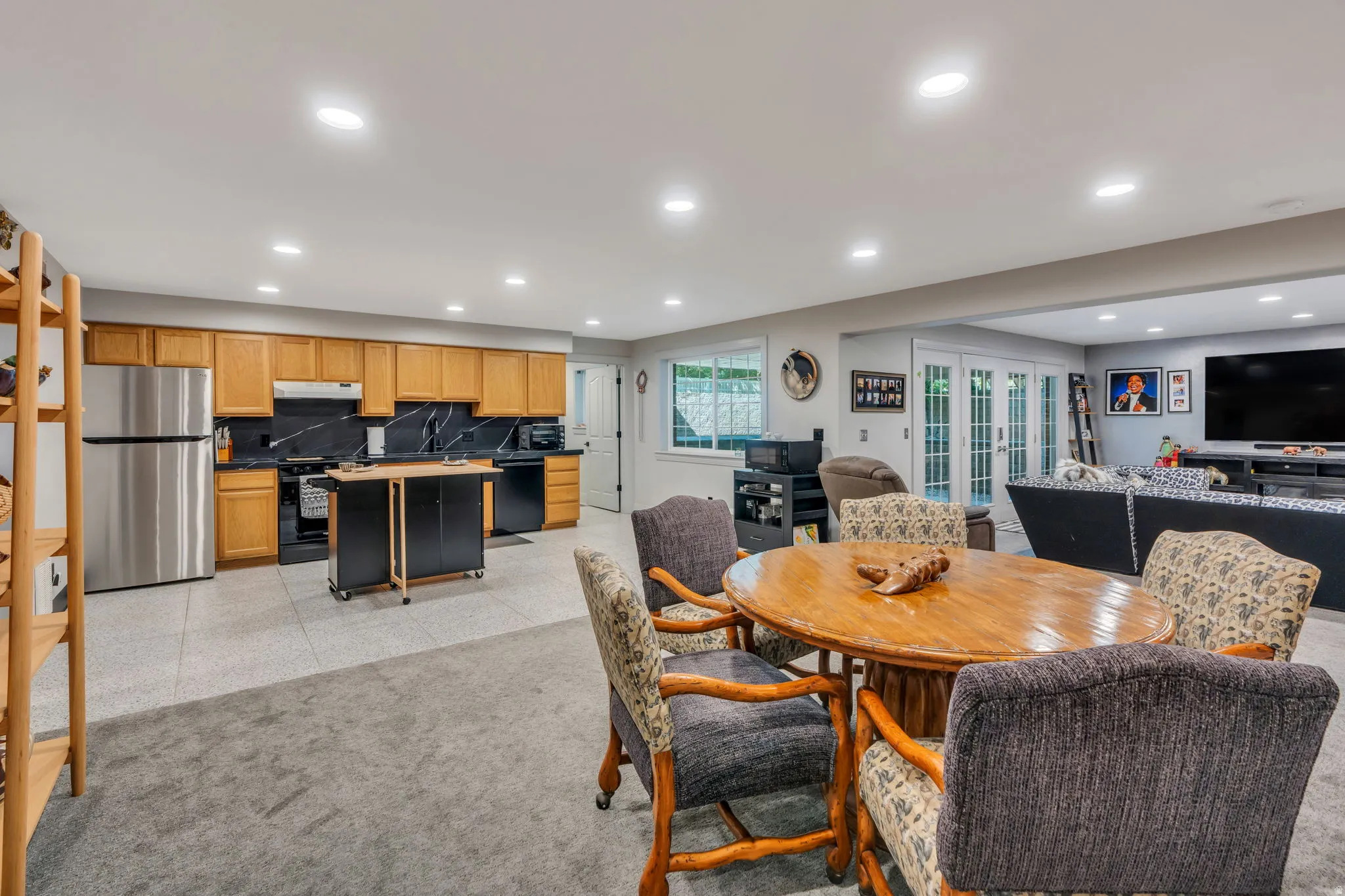 Open-concept living space featuring a full kitchen with light wood cabinetry, stainless steel refrigerator, and black appliances