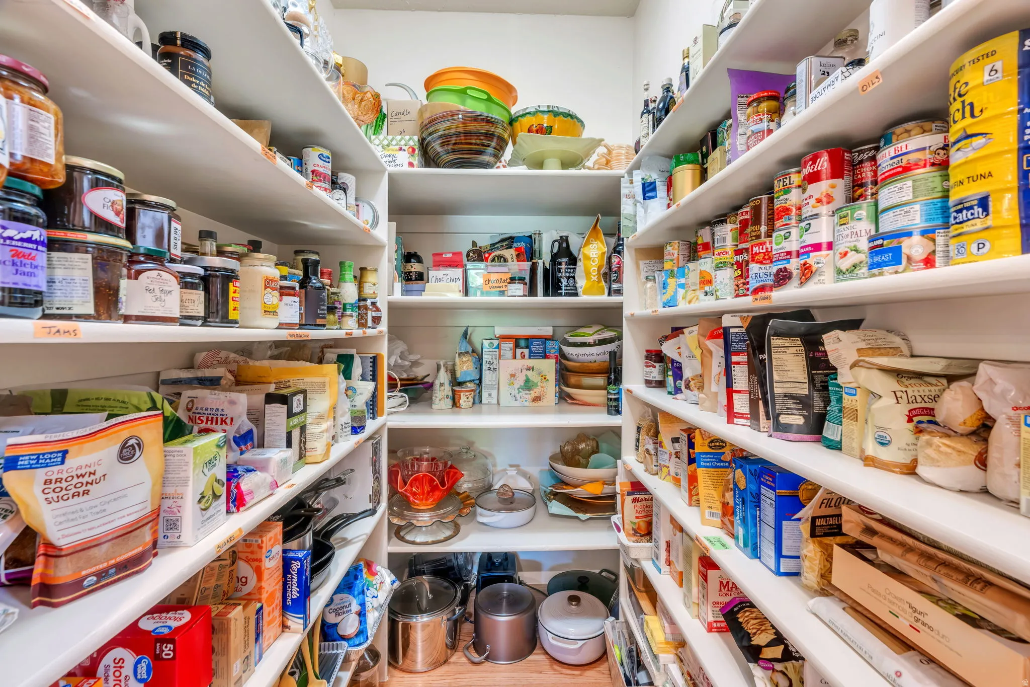 Walk-in pantry featuring extensive built-in shelving, white shelf finishes, and wood-finish flooring