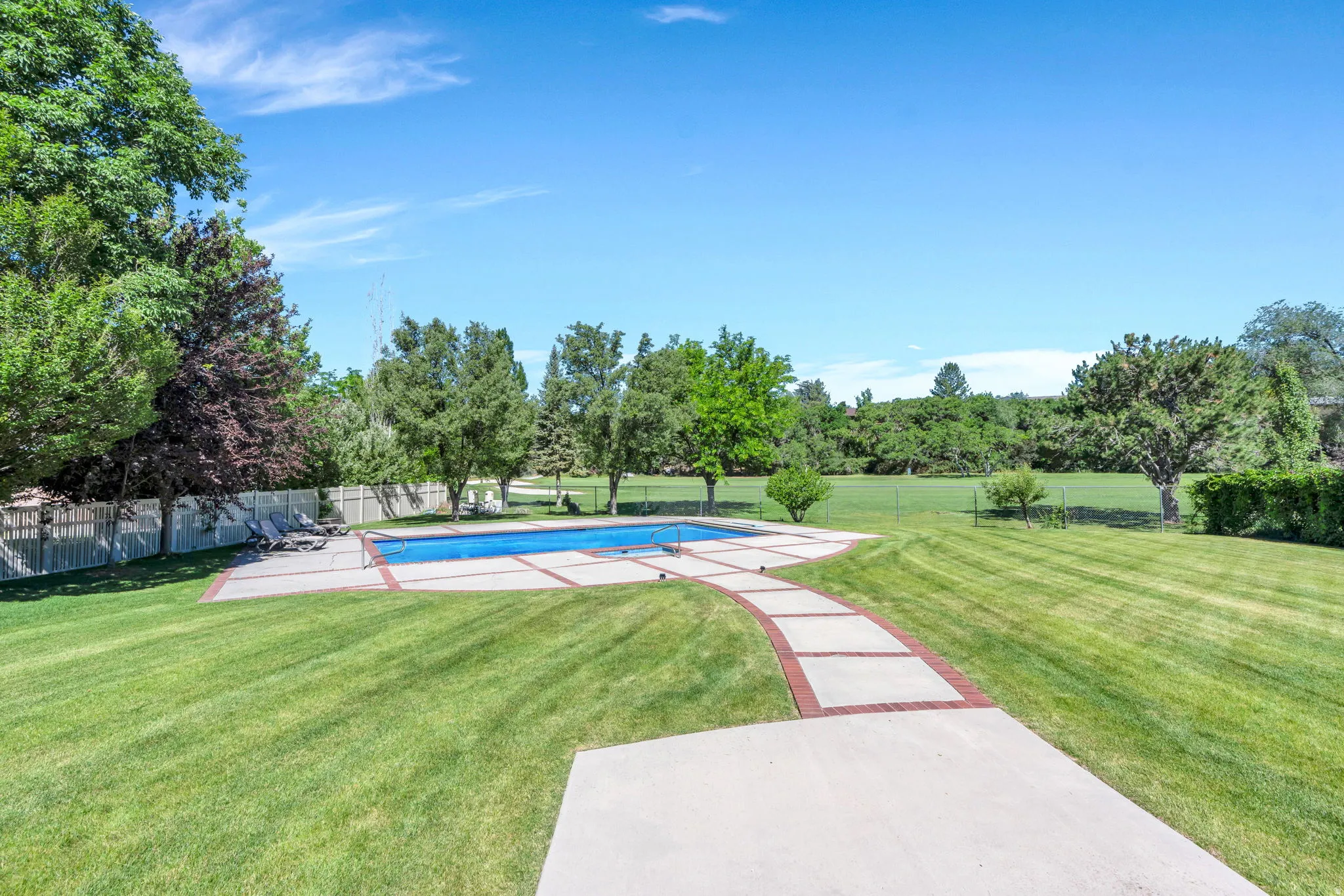 Expansive green lawn with a swimming pool, bordered by a concrete patio and a red brick pathway
