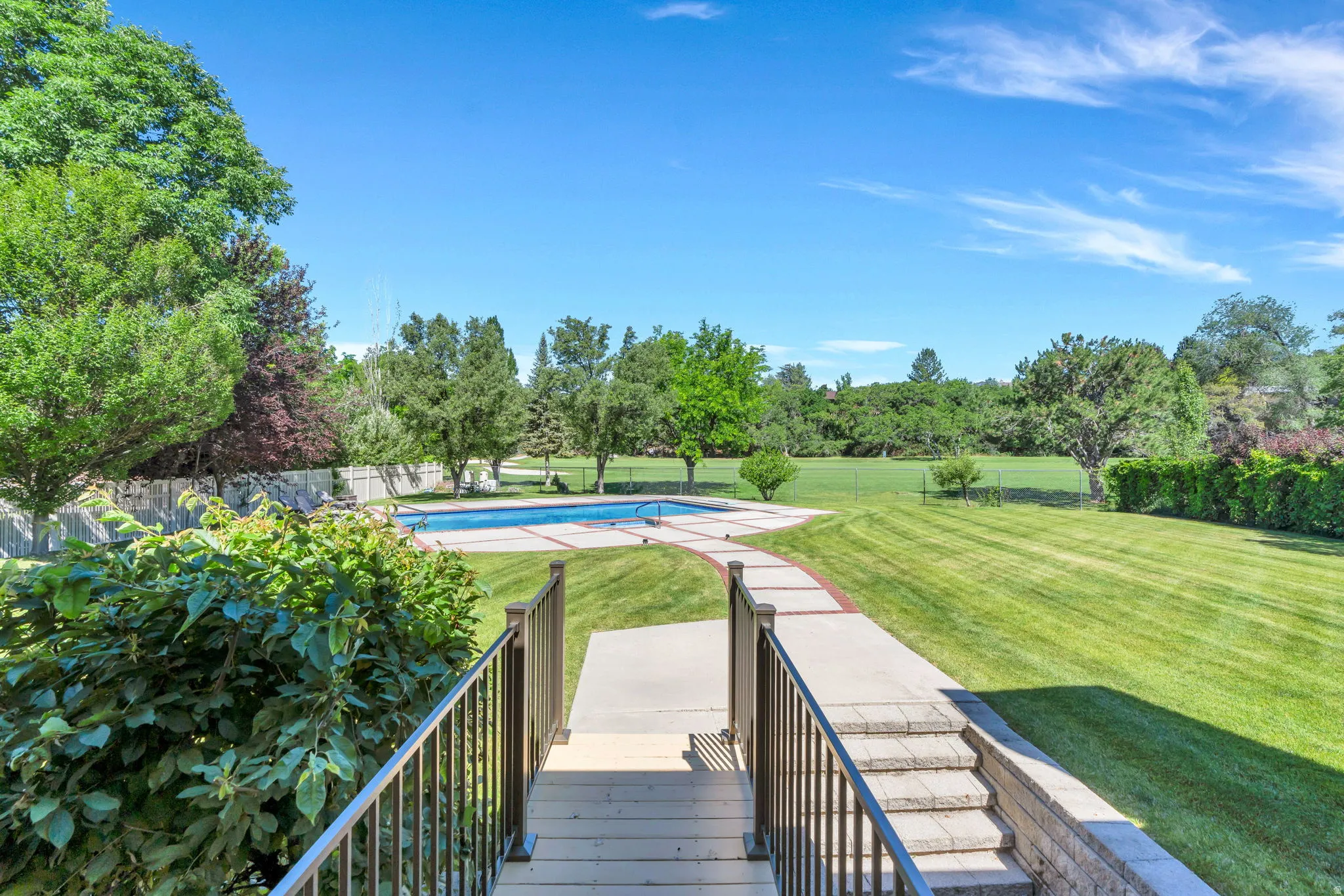 Expansive green lawn with a rectangular swimming pool, surrounding concrete patio, mature trees, and a stone retaining wall