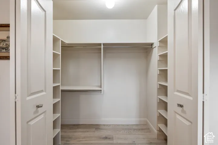 Recessed closet with light wood-finish flooring, built-in shelving, and hanging rods