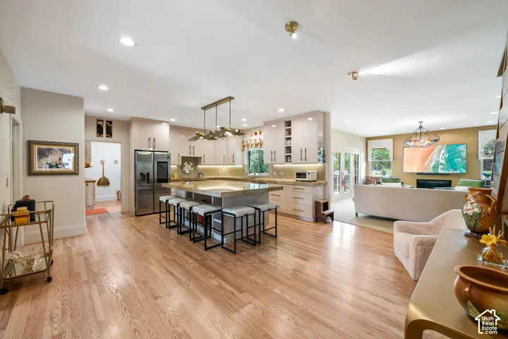 Open-concept living area featuring wood-finish flooring throughout, a kitchen island with seating, recessed lighting, and a kitchen with light-toned cabinetry