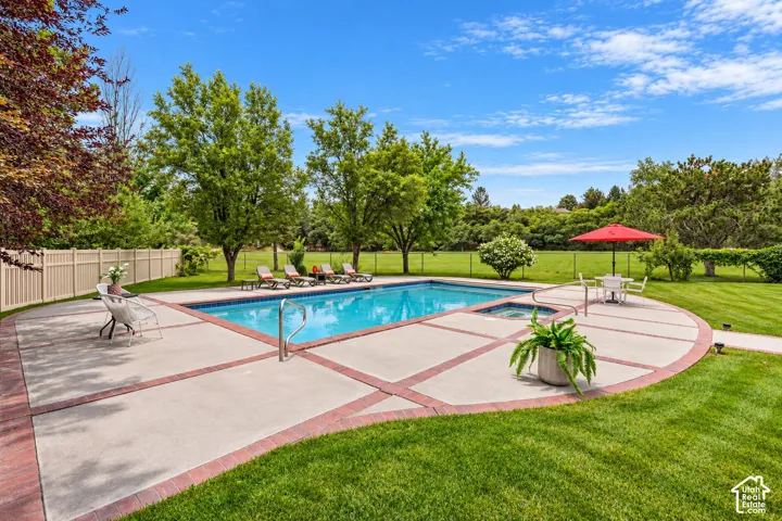In-ground swimming pool with an integrated spa, surrounded by a concrete patio with brick accents, expansive lawn, and mature trees