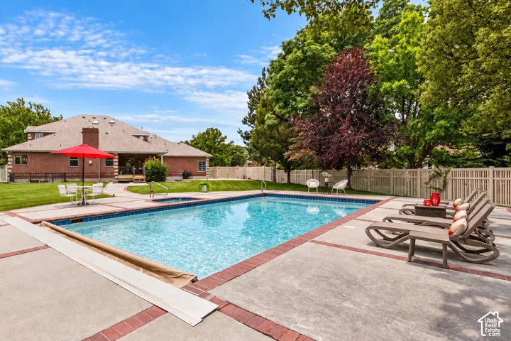 Expansive outdoor pool area featuring a rectangular pool, integrated spa, and concrete decking with brick accents