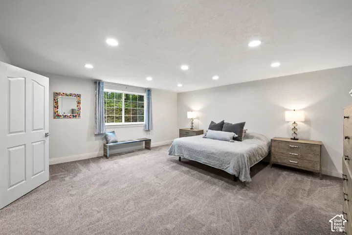 Recessed ceiling lighting, light gray wall finishes, light gray carpeting, and a window with natural light. Basement primary room