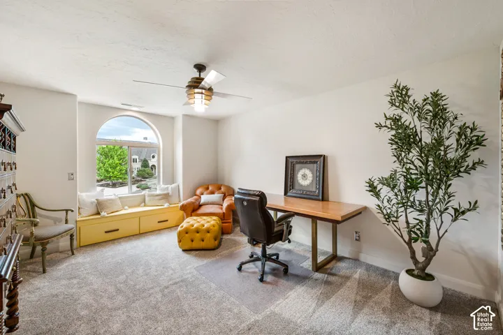 Arched window with a built-in window seat, textured carpet, and a ceiling fan