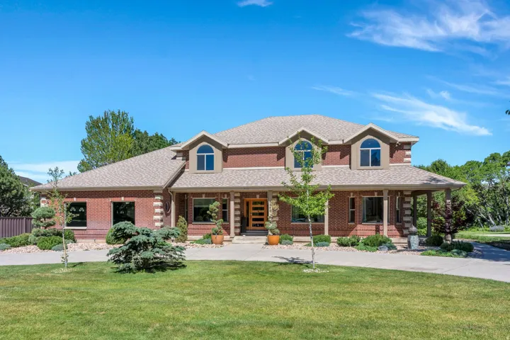 Stately brick residence featuring multiple gabled dormers, a covered front porch with substantial columns, and a paved driveway
