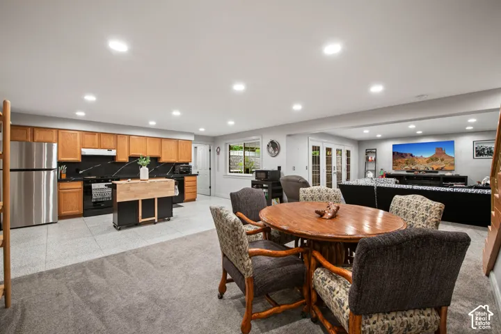 Recessed lighting, wood-finish cabinetry, stainless steel refrigerator, black cooktop, and glass-paneled French doors