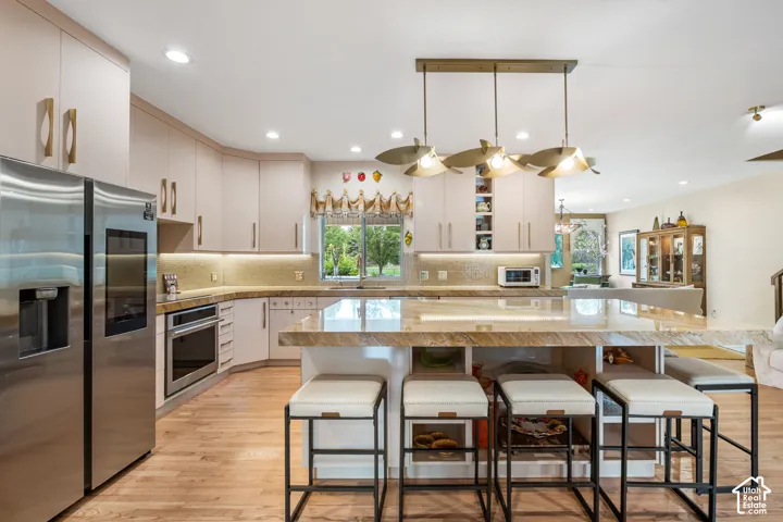 Integrated kitchen featuring wood-finish flooring, stainless steel appliances, upper and lower cabinetry, a center island with seating, and recessed lighting