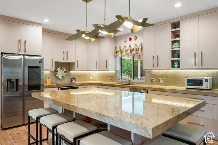 Light-toned cabinetry, stainless steel refrigerator, undermount sink, gold-toned tiled backsplash, and recessed lighting