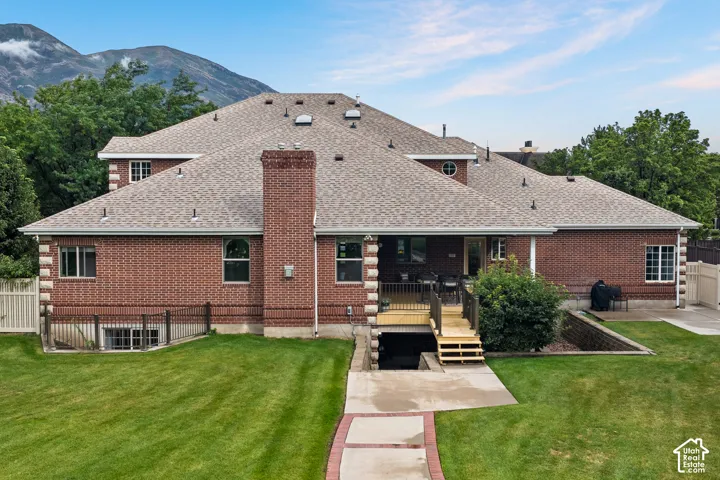 Brick exterior with a prominent brick chimney,shingle roof, deck with stairs, and a concrete patio