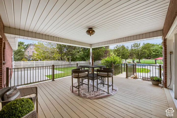 Main floor covered patio with wood-finish decking, black metal railings, and a hanging light fixture