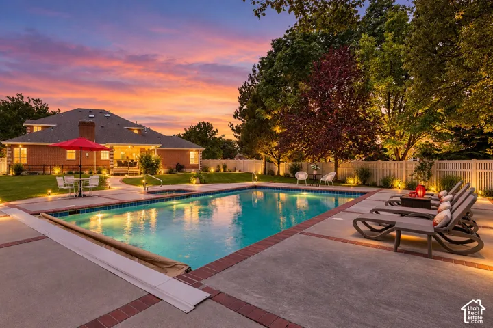 Expansive backyard featuring a large in-ground swimming pool with integrated lighting, a spacious concrete patio, and a brick-accented border