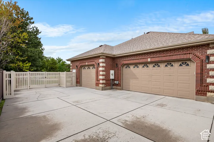 Red brick exterior with stone accents, concrete driveway, two garage doors with arched windows, and a light-colored fence with a gate