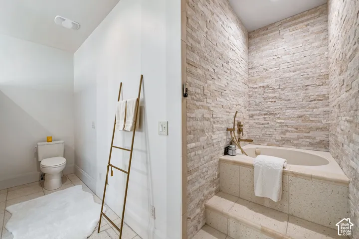 Built-in soaking tub with a stone tile surround, complemented by a floor-to-ceiling stacked stone accent wall. Doubles as a cold plunge!