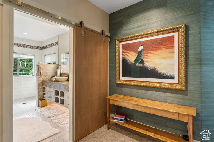 Bathroom featuring a wood-finish barn door, white tiled walls, a vanity with a vessel sink, and a window