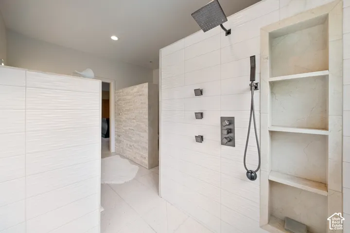 Shower with matte black fixtures, textured white tile walls, recessed shelving, and a handheld showerhead