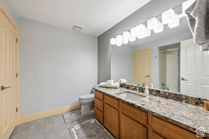 Wood-finish vanity with dual sinks, a stone-finish countertop, and a large wall-mounted mirror with integrated lighting