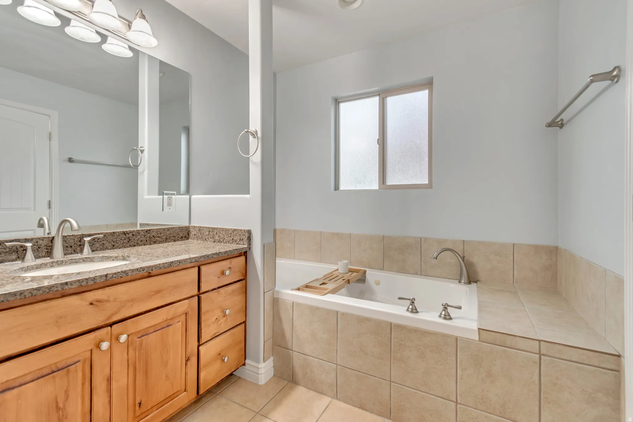 Bathroom featuring a dual-sink vanity with a granite-style countertop, wood-finish cabinetry, and brushed nickel hardware