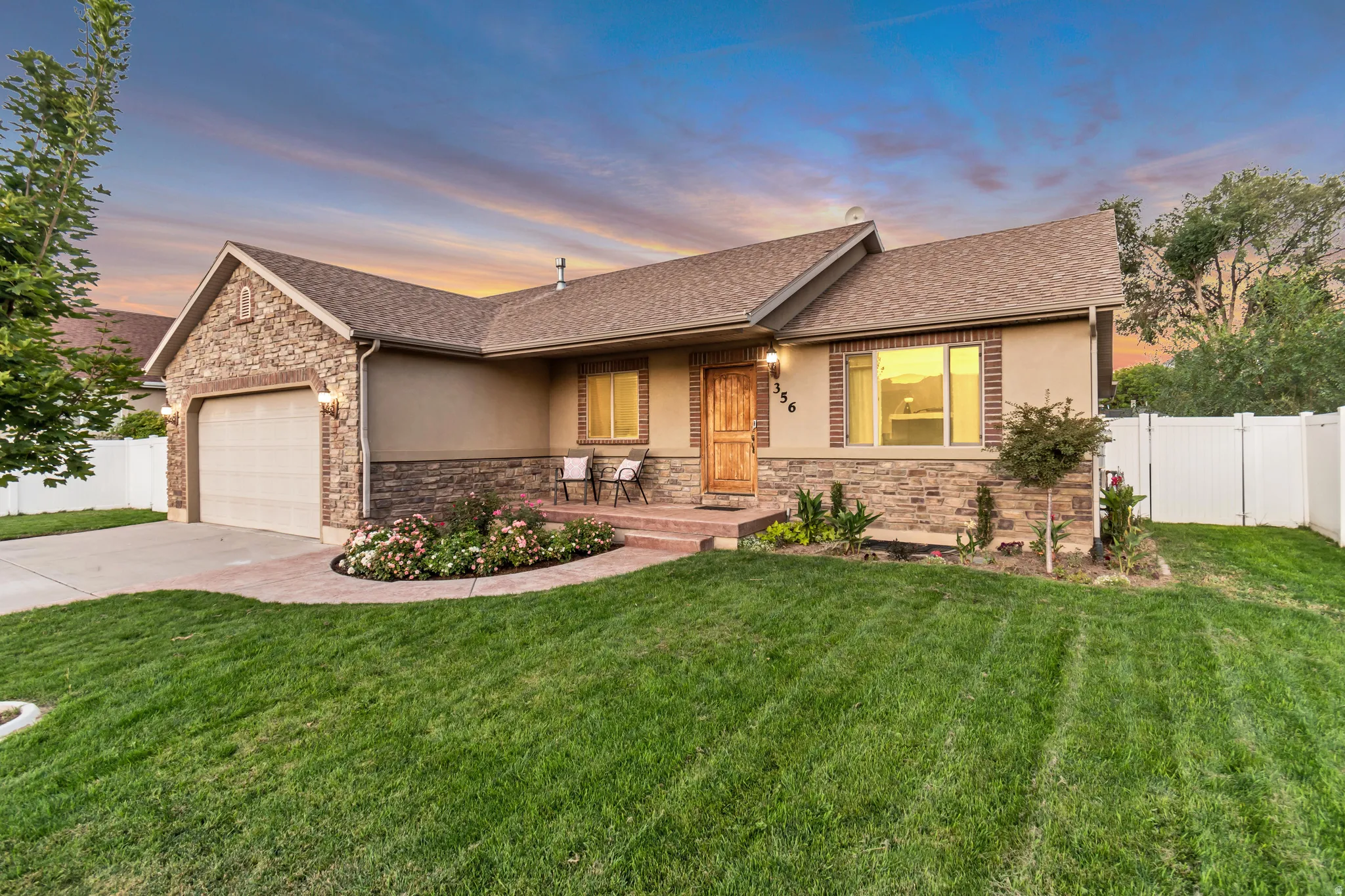 Stone and stucco exterior with brick accents, an attached garage, a covered entry, and a fully fenced yard