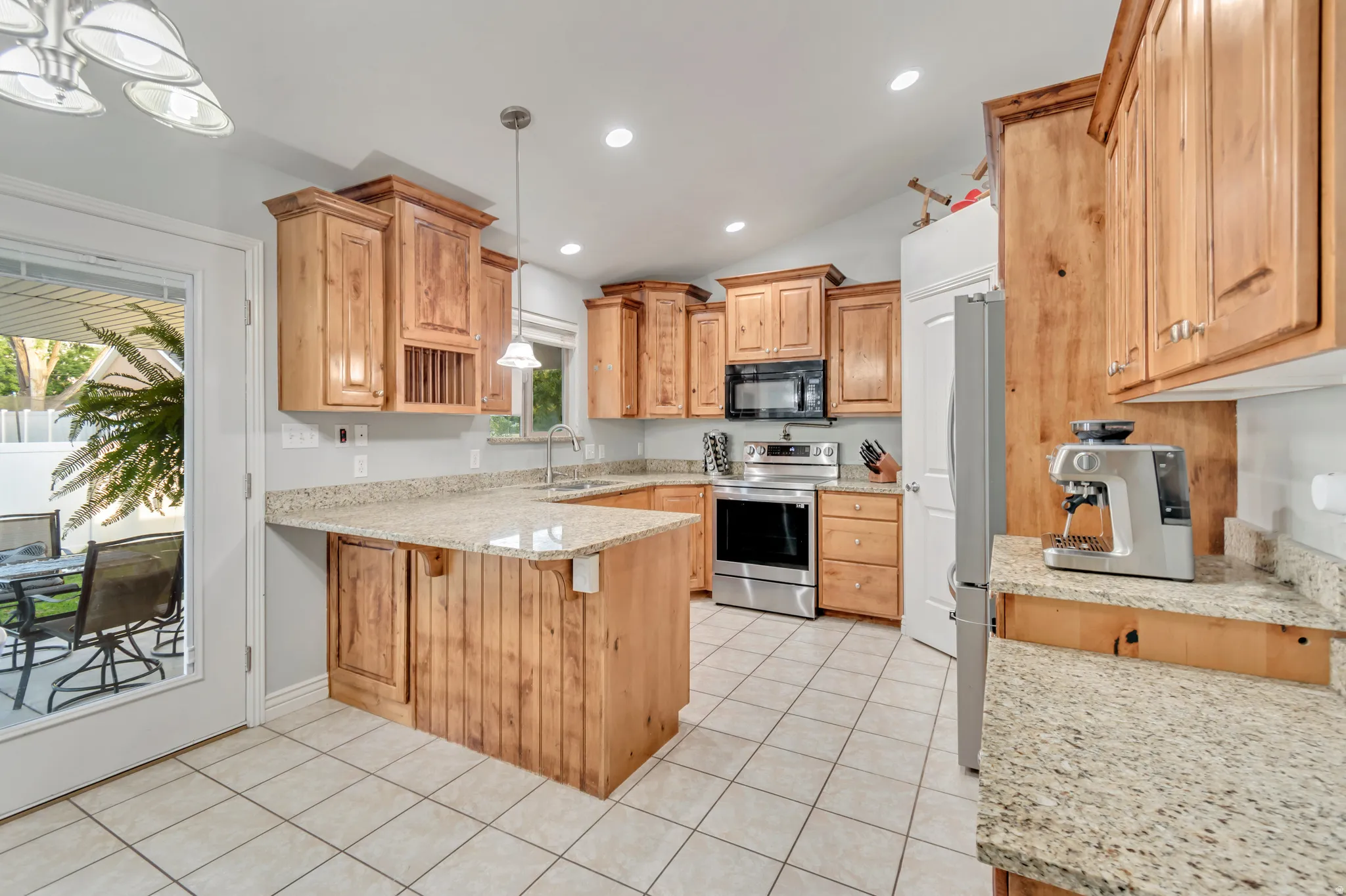 Kitchen featuring wood cabinetry, light-toned granite countertops, stainless steel appliances, and tile flooring