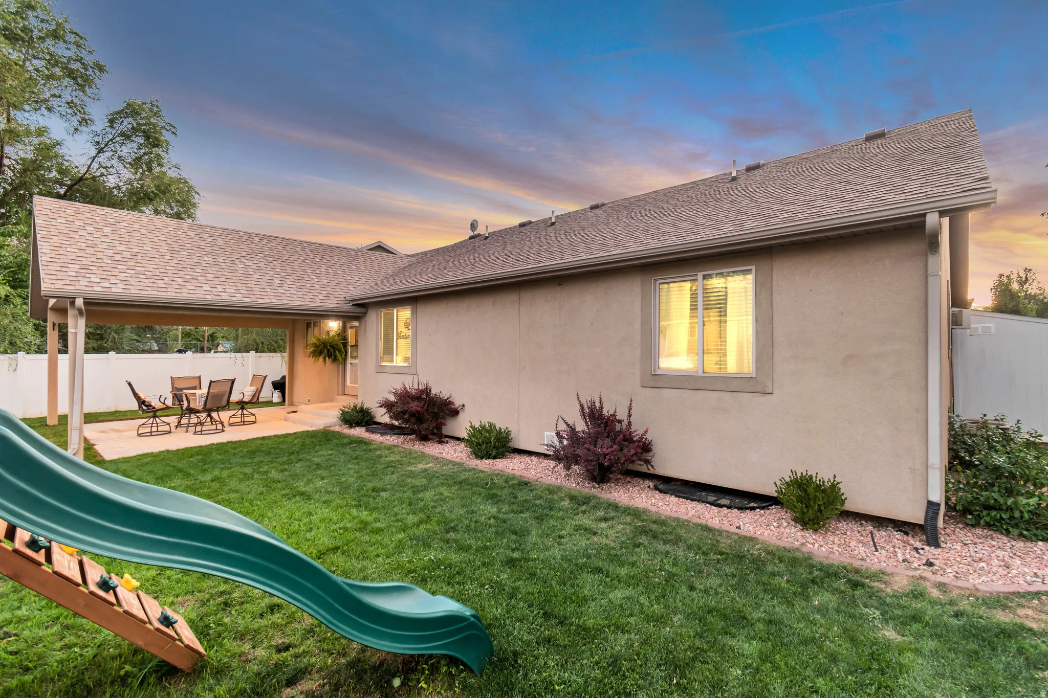 Expansive green lawn with a covered patio area, stucco exterior, and mature landscaping