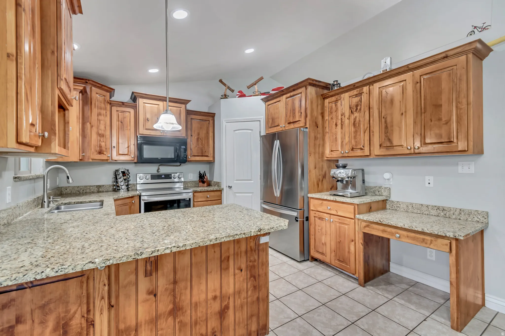 Well-appointed kitchen featuring granite countertops, wood cabinetry, stainless steel appliances, a built-in desk area, and tile flooring