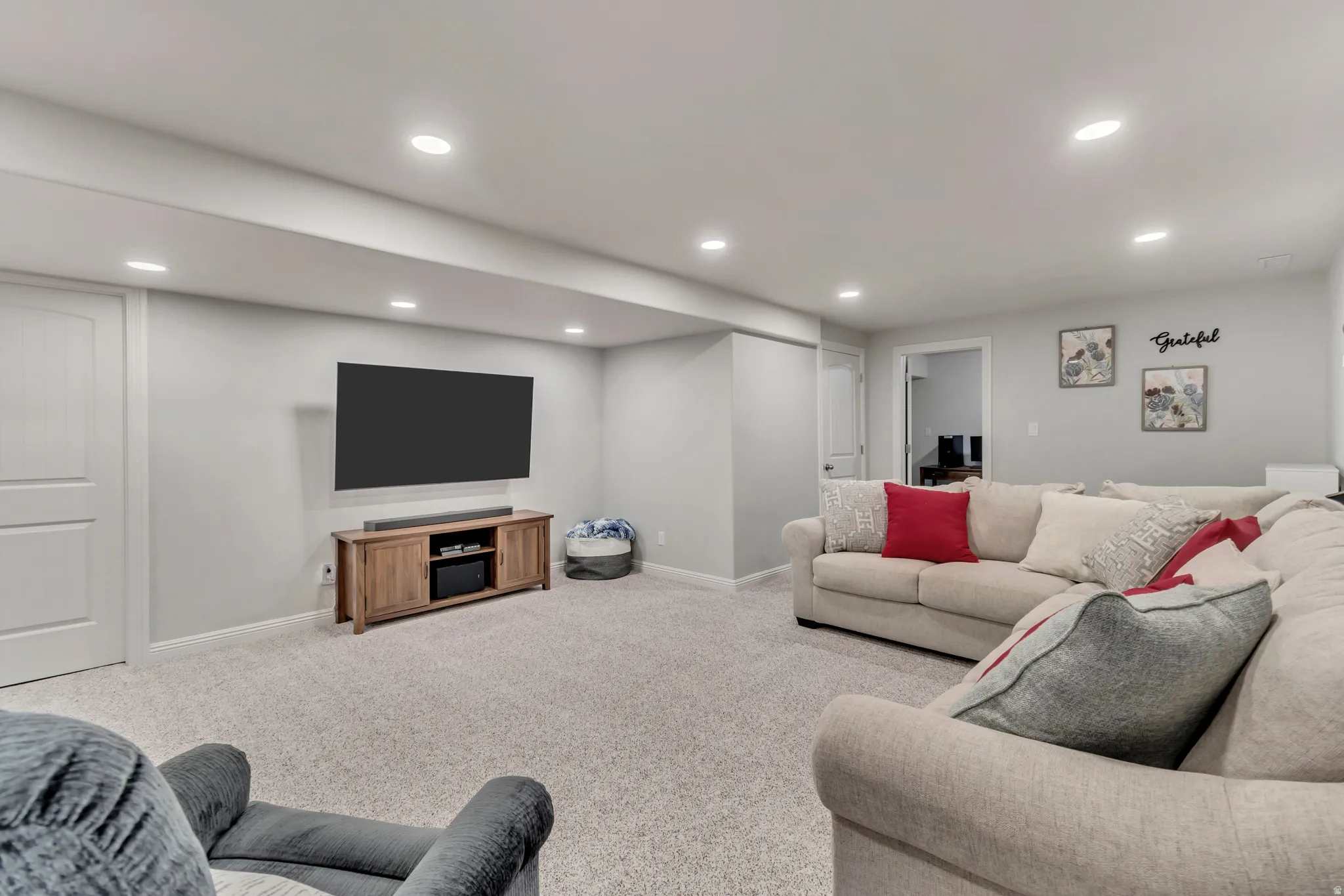 Spacious entertainment area featuring light gray walls, recessed lighting, and soft gray carpeting