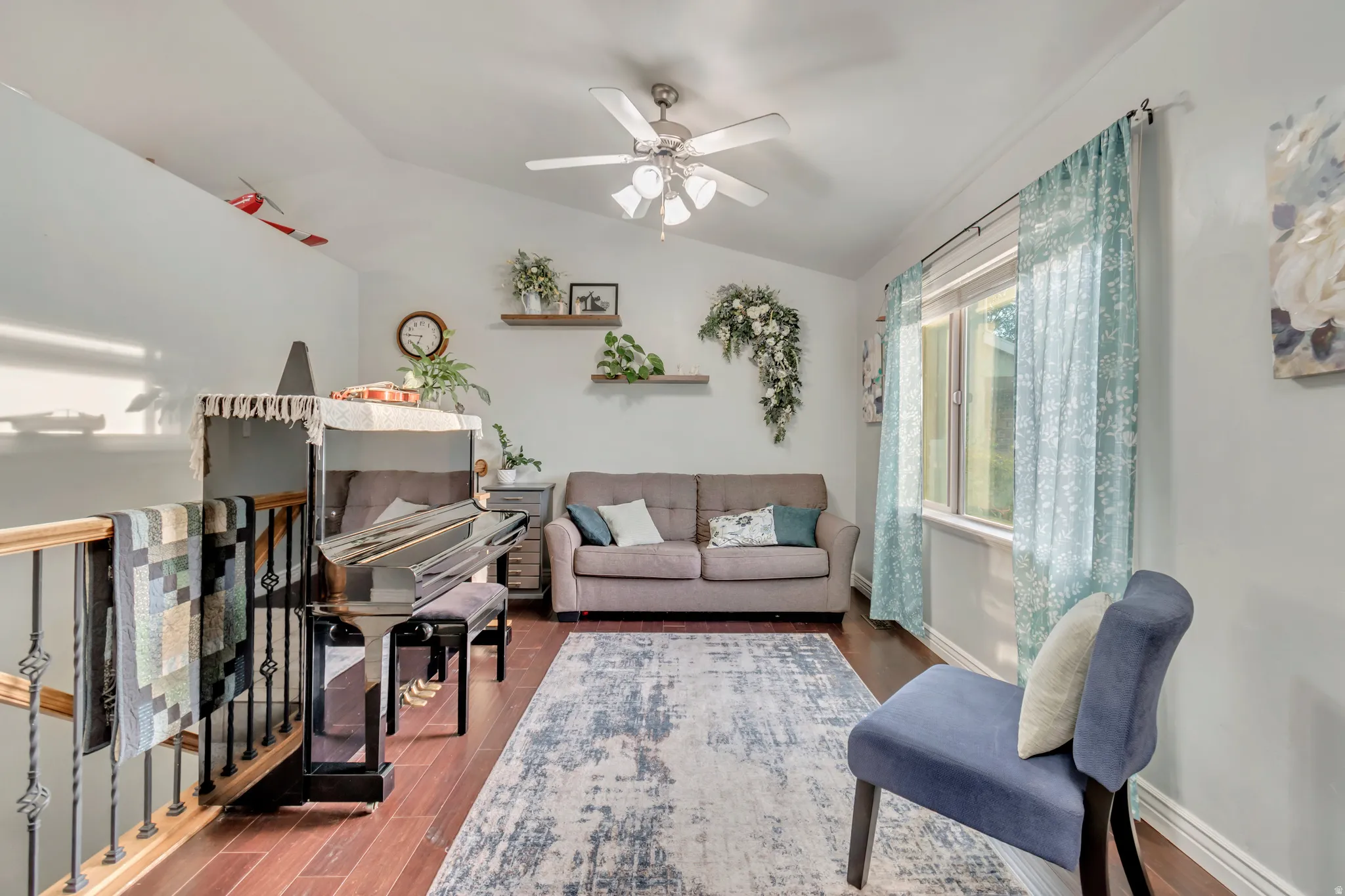 Upper-level living area with vaulted ceiling, wood-finish flooring, a ceiling fan, and a large window