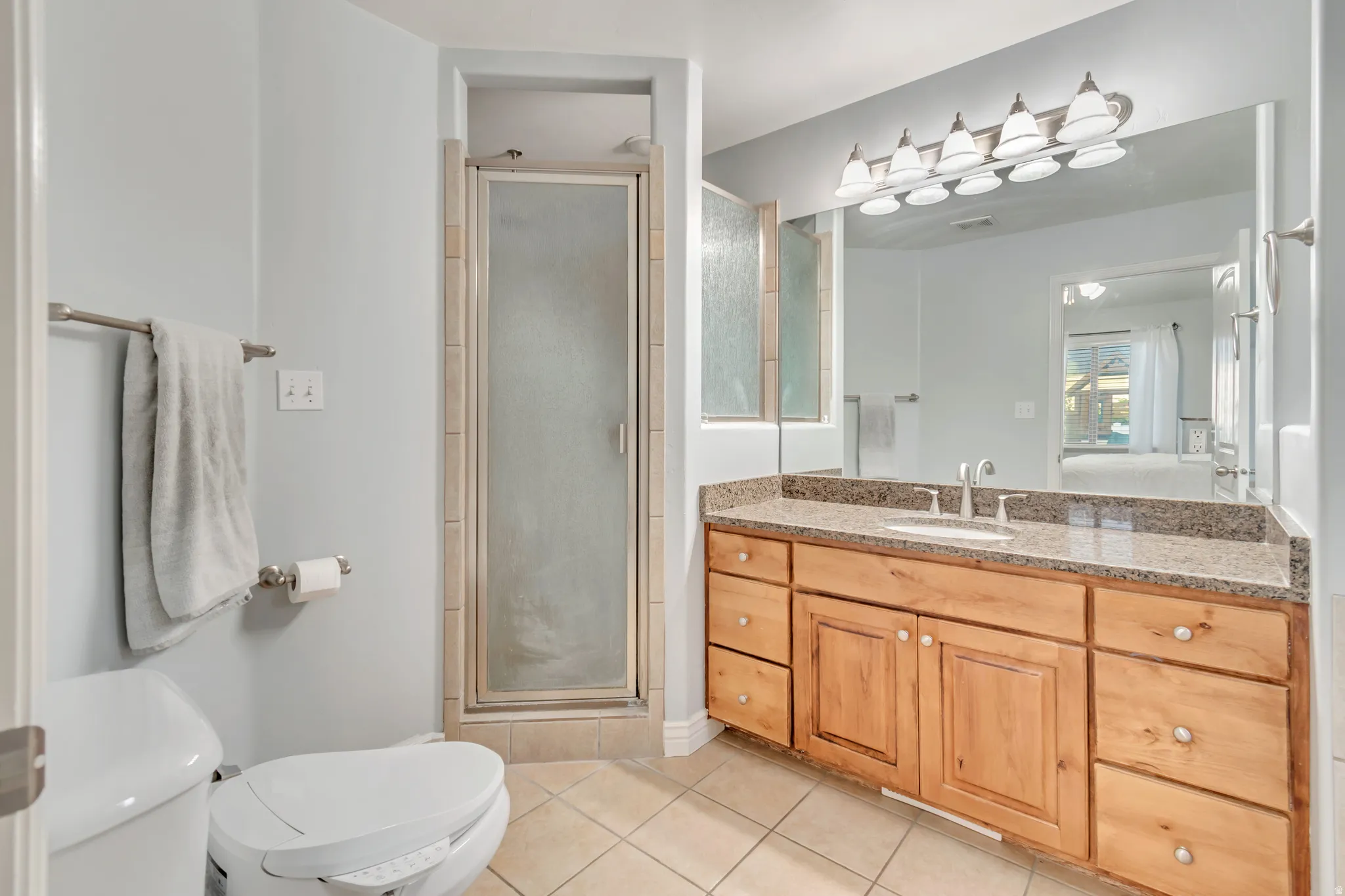 Bathroom featuring a wood vanity with a granite countertop and integrated sink, a glass-enclosed shower, a large wall-mounted mirror, and tile flooring