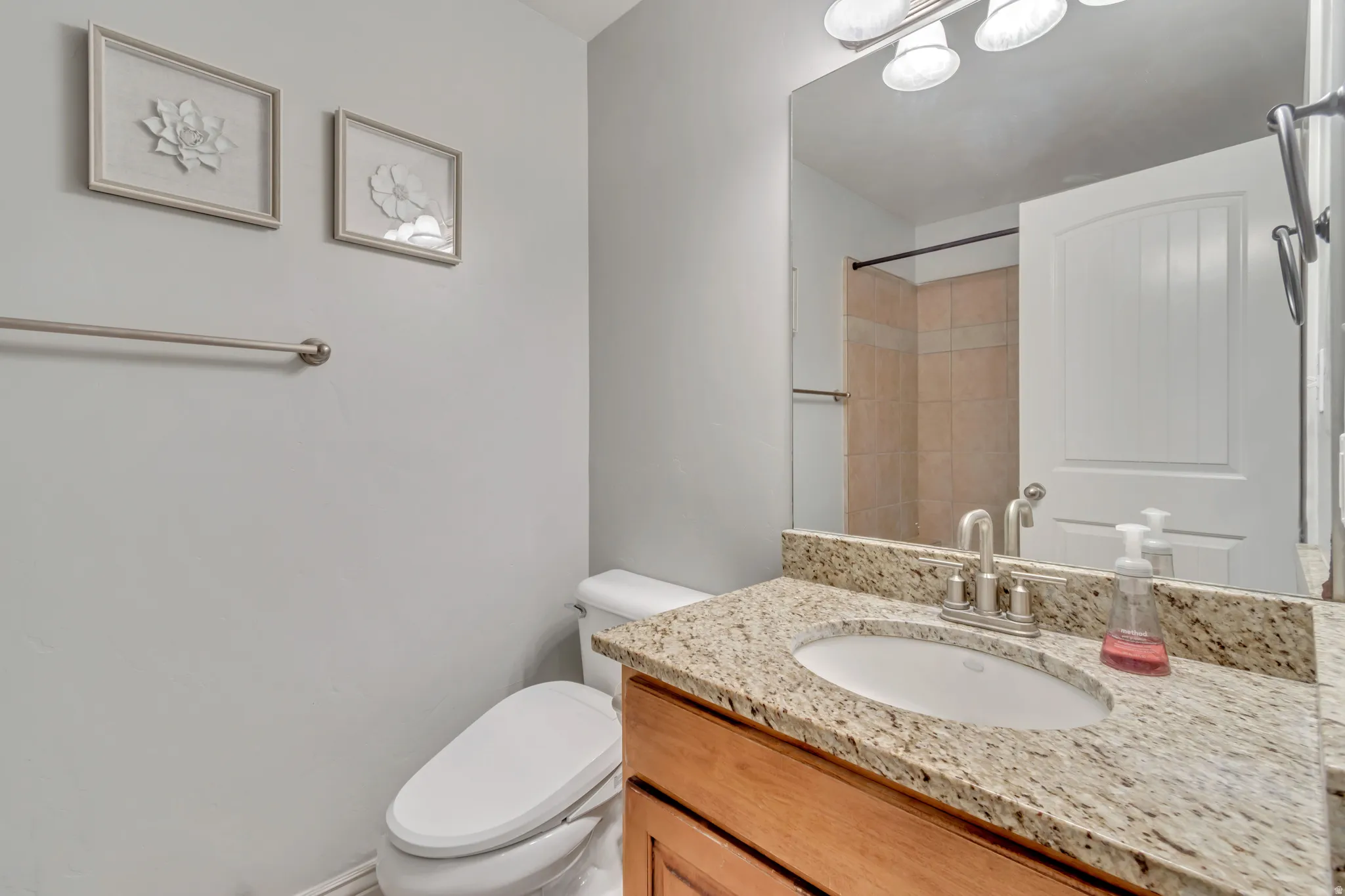 Bathroom featuring a granite countertop vanity with an undermount sink, a large wall-mounted mirror, and a three-light fixture overhead