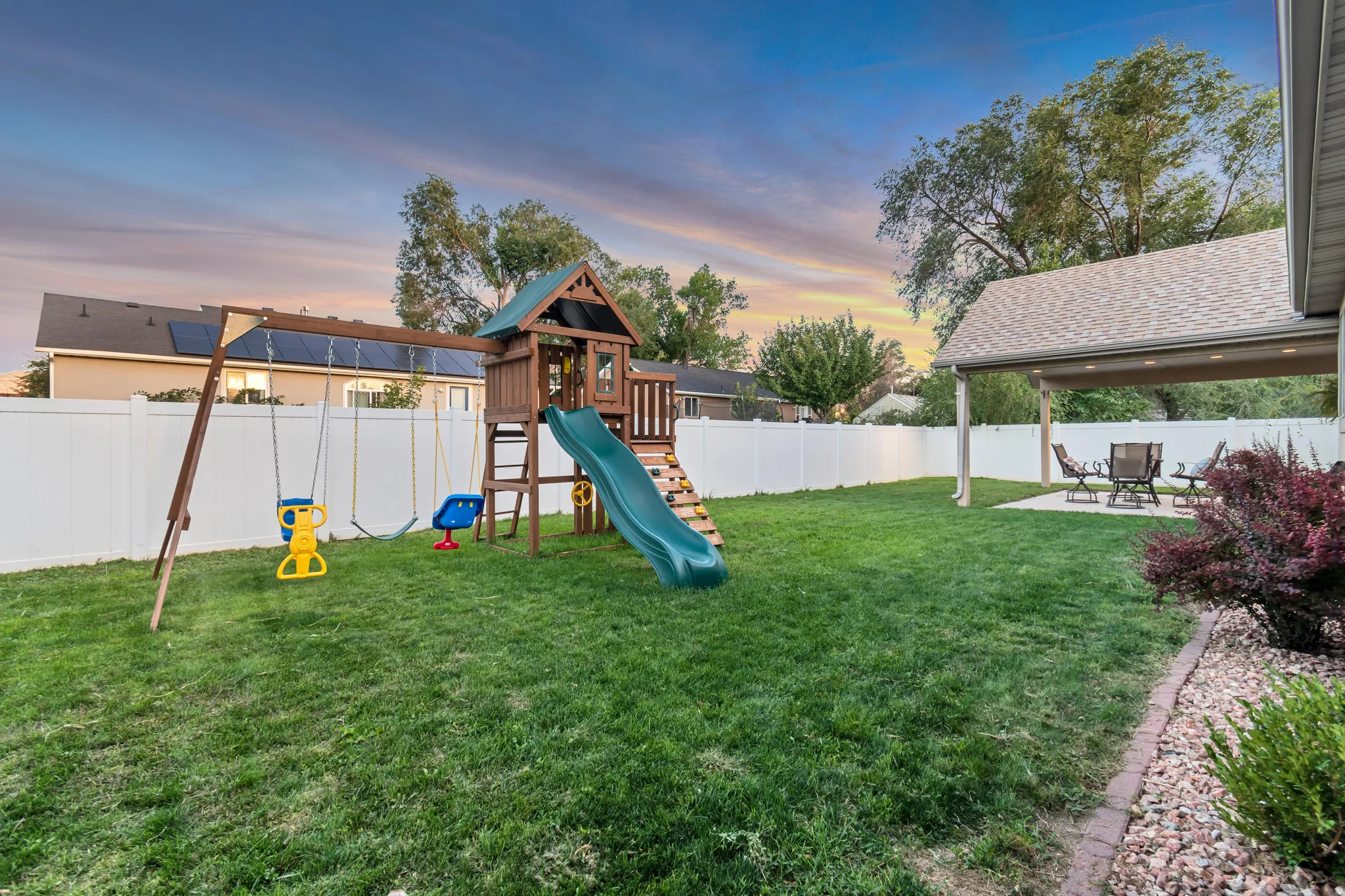Expansive backyard featuring a covered patio, manicured lawn, and white privacy fencing