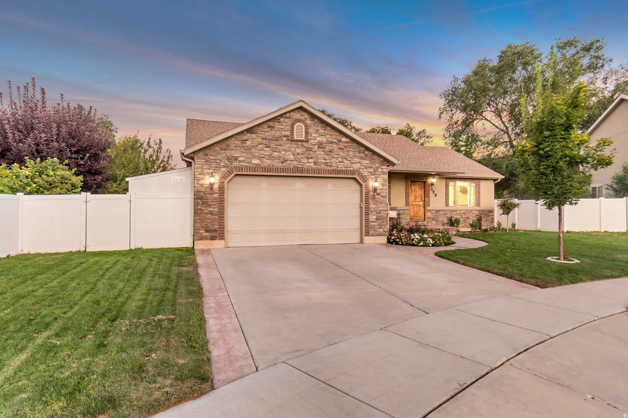 Stone-accented exterior featuring a two-car garage, concrete driveway with paver border, and a well-maintained lawn