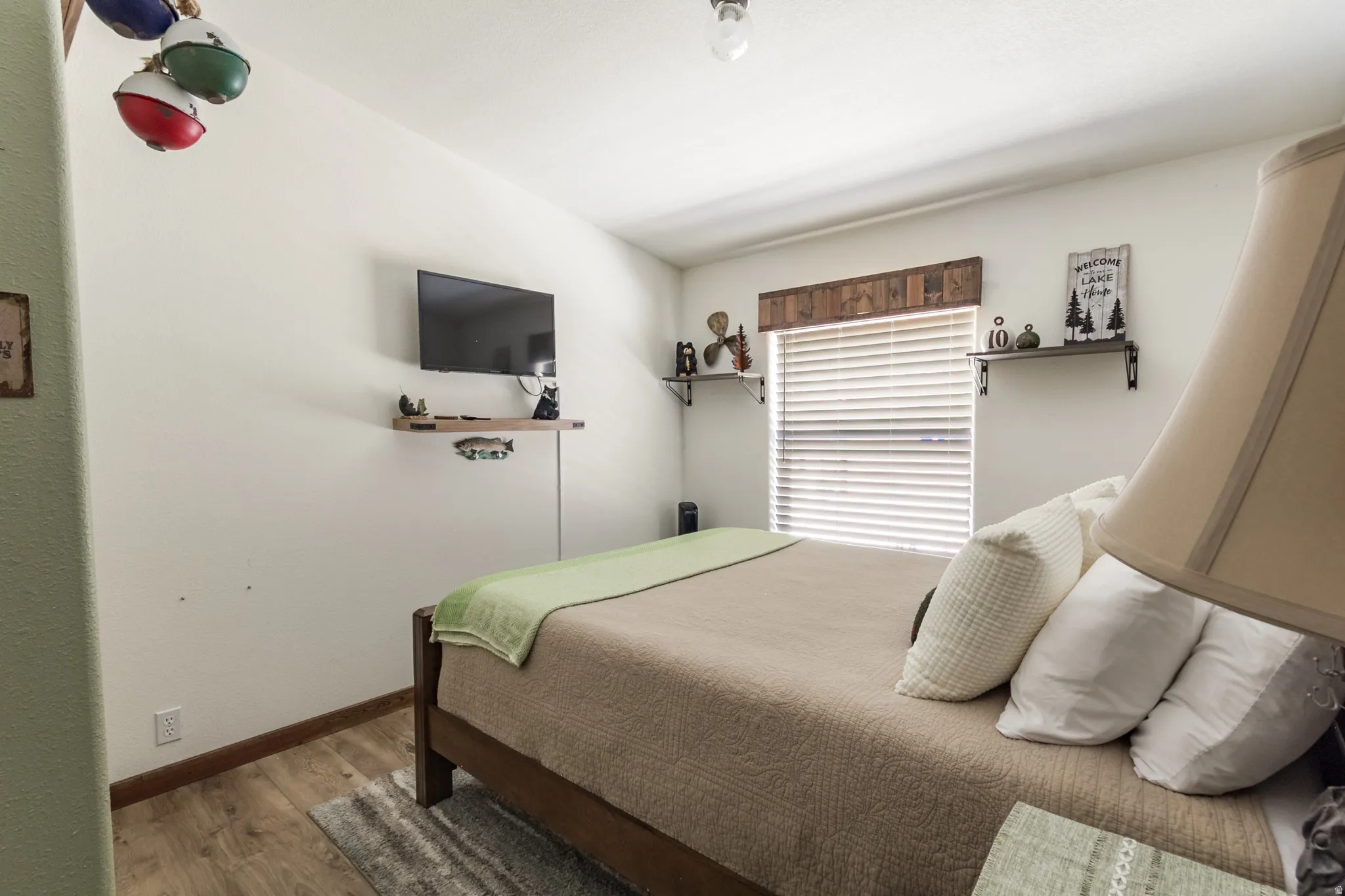 Bedroom featuring wood-finish flooring, light-toned walls, and a window with blinds