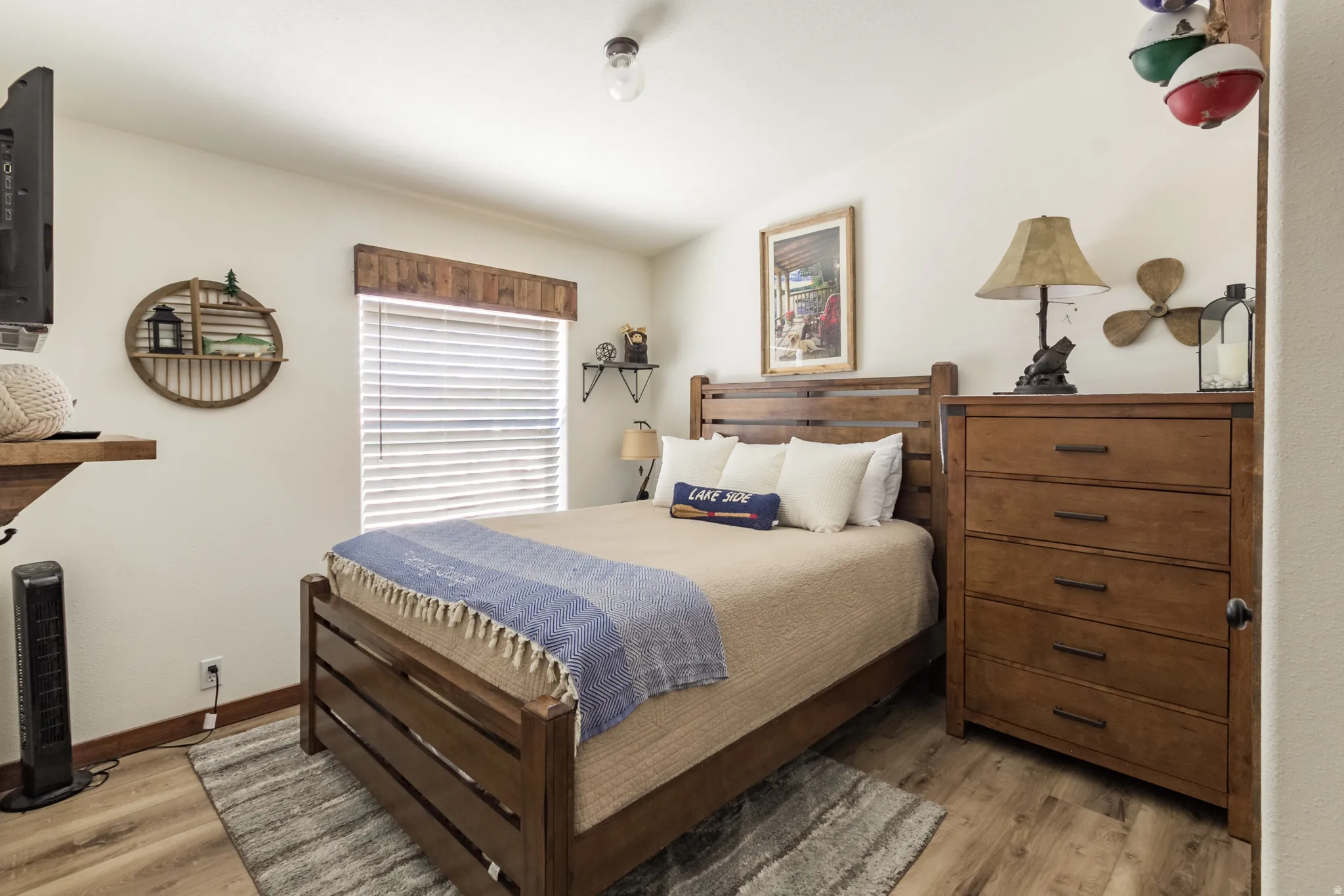 Bedroom featuring wood-finish flooring, a window with horizontal blinds and a wood valance, and neutral wall paint
