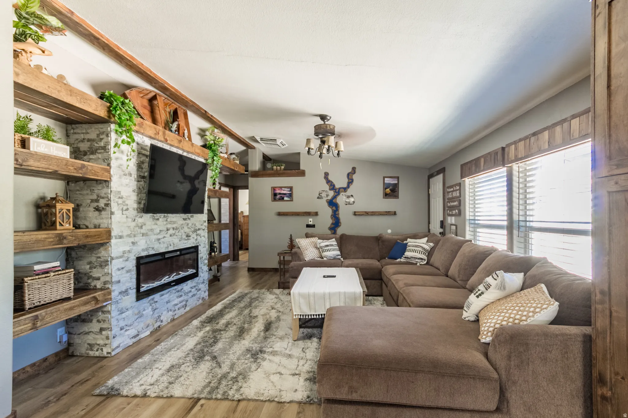Living area featuring wood-finish flooring, a white stone-clad fireplace with an electric insert, and built-in wood shelving